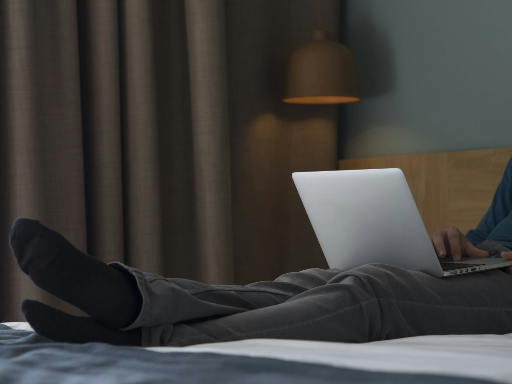 Ein Mann sitzt mit seinem Laptop auf einem Hotelbett.