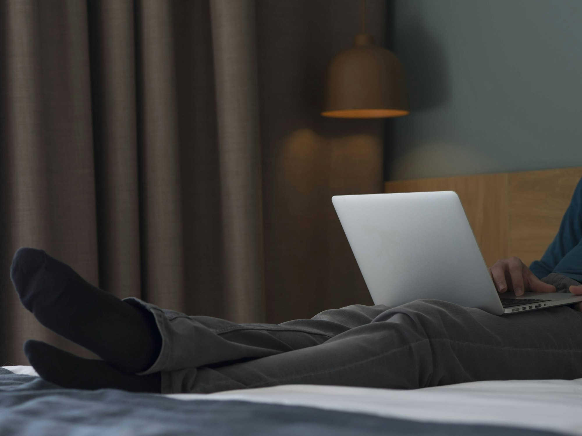 Ein Mann sitzt mit seinem Laptop auf einem Hotelbett.