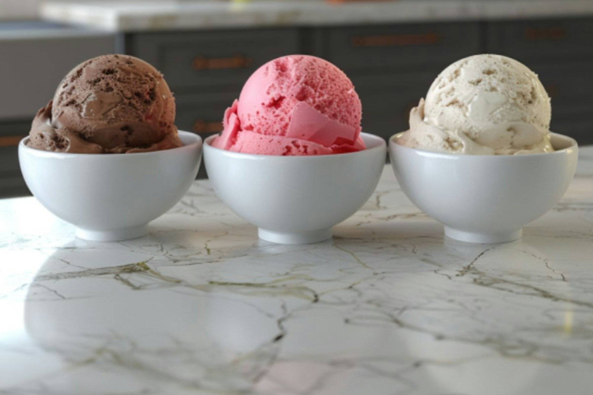 Drei Schalen mit Eis (Schoko, Erdbeere und Zitronen) auf einer Kücheninsel