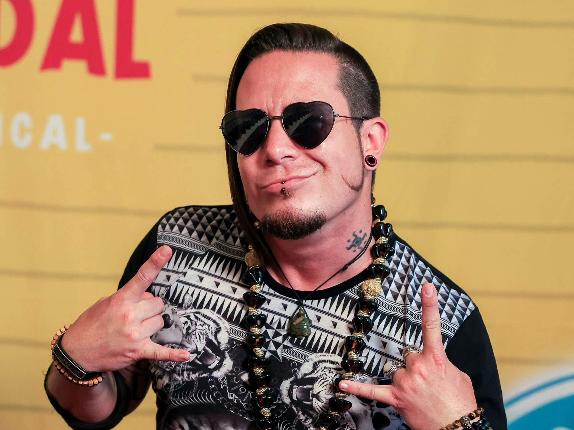 Ein Mann in auffälligen Klamotten, mit Armbändern und Sonnenbrille posiert von der Kamera.