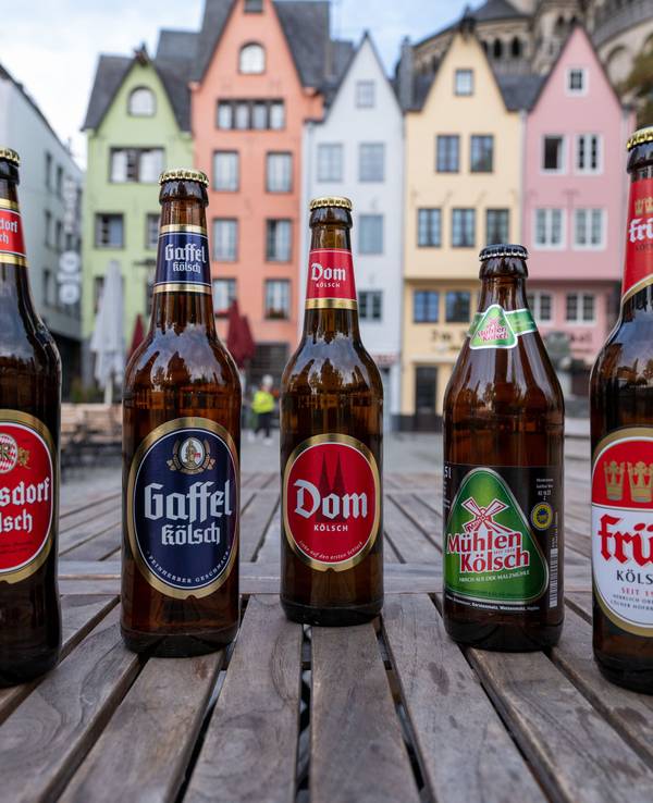 Fünf Bierflaschen von unterschiedlichen Marken stehen auf einem Tisch nebeneinander.