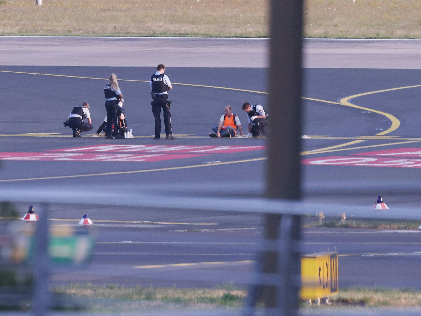 Polizisten stehen am 13. Juli 2023 auf dem Flugfeld in Düsseldorf und versuchen Aktivisten der Gruppe „Letzte Generation“ am Flughafen vom Asphalt zu lösen, nachdem sie sich festgeklebt haben.