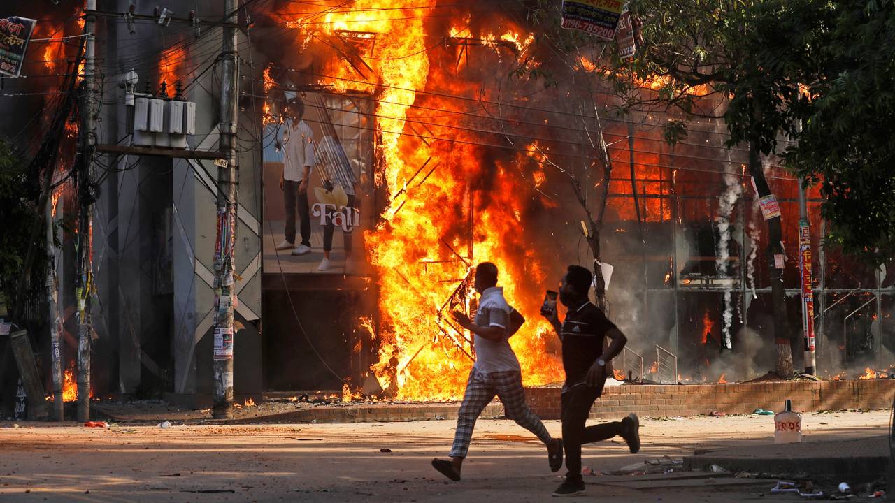Männer rennen an einem Einkaufszentrum vorbei, das von Demonstranten während einer Kundgebung gegen Premierministerin Hasina und ihre Regierung angezündet wurde.