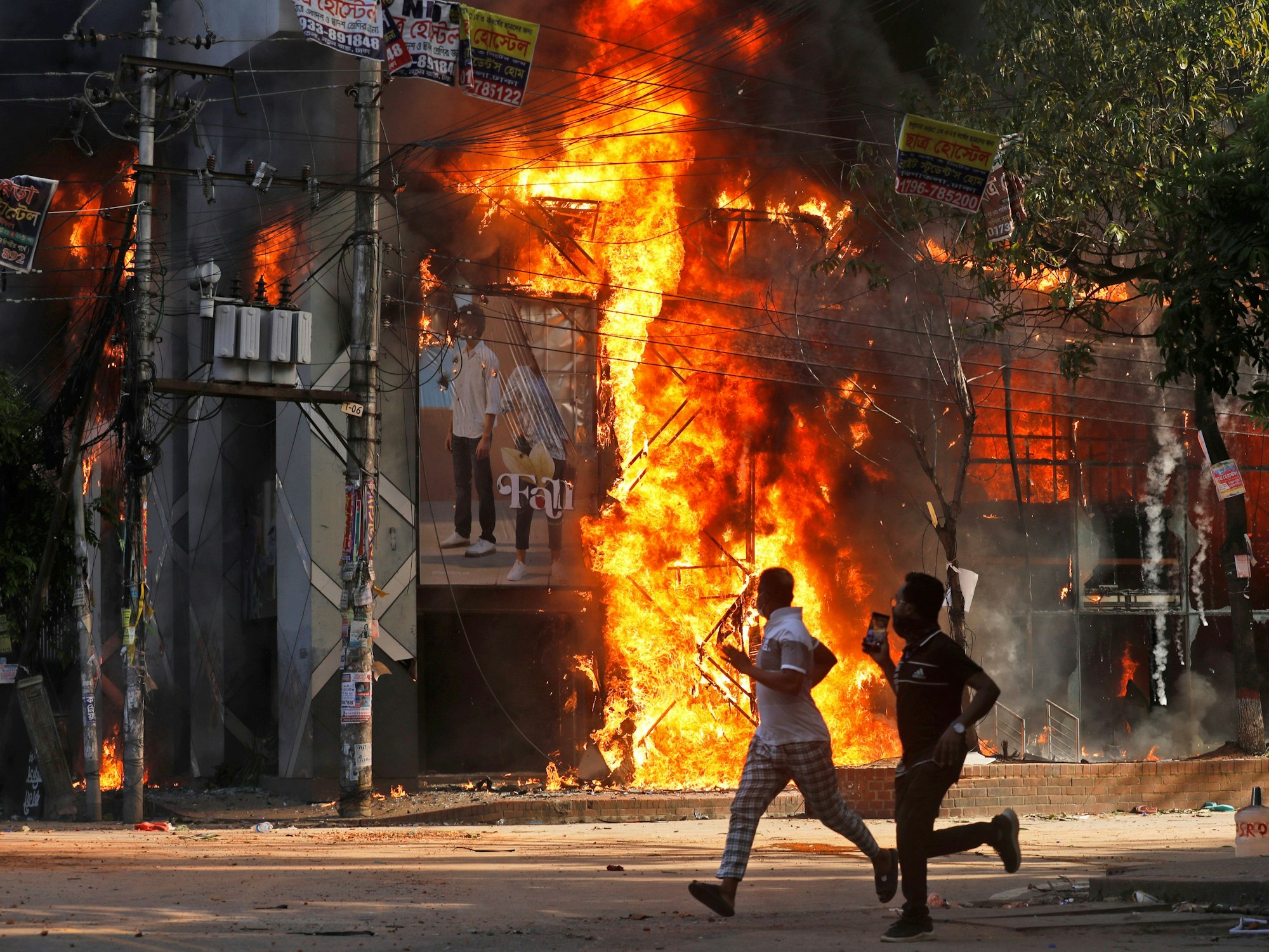 Männer rennen an einem Einkaufszentrum vorbei, das von Demonstranten während einer Kundgebung gegen Premierministerin Hasina und ihre Regierung angezündet wurde.