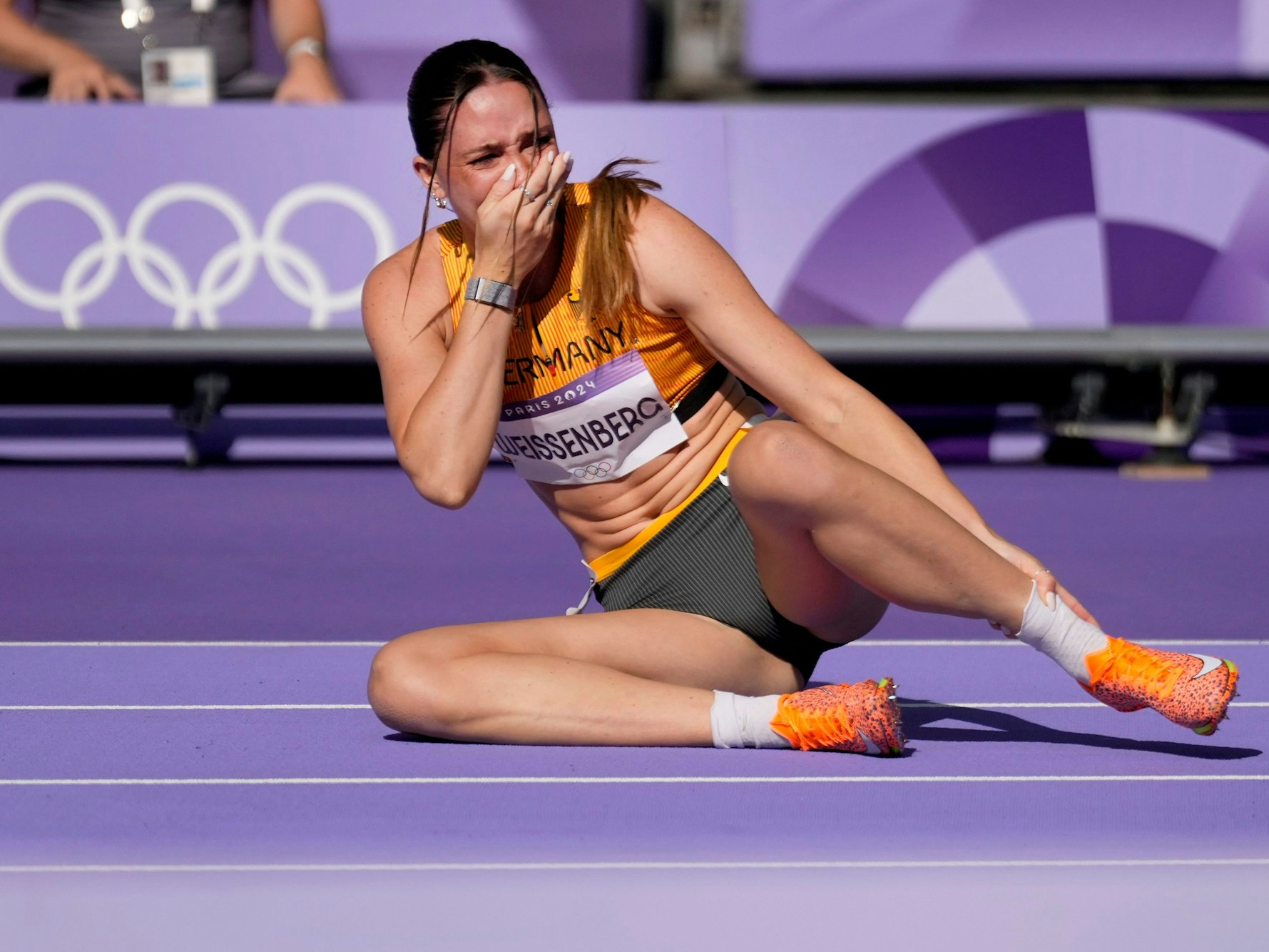 Sophie Weißenberg sitzt auf der Laufbahn, mit der linken Hand hält sie sich den Fuß, mir der rechten die Hand geschockt vor den Mund.