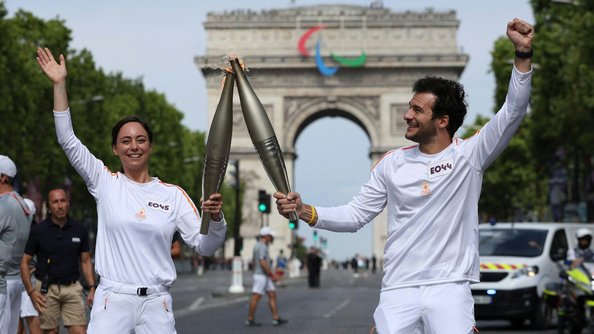 Eine Frau und ein Mann halten vor dem Triumphbogen in Paris die olympische Fackel hoch.