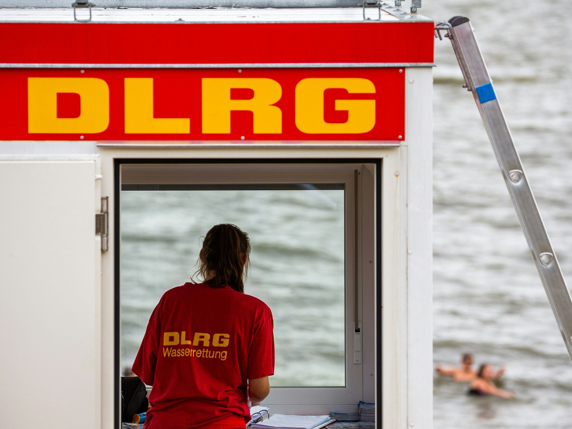 Eine Rettungsschwimmerin der DLRG (Deutsche Lebens-Rettungs-Gesellschaft) steht vor dem Fenster eines Wachturms (Symbolfoto).