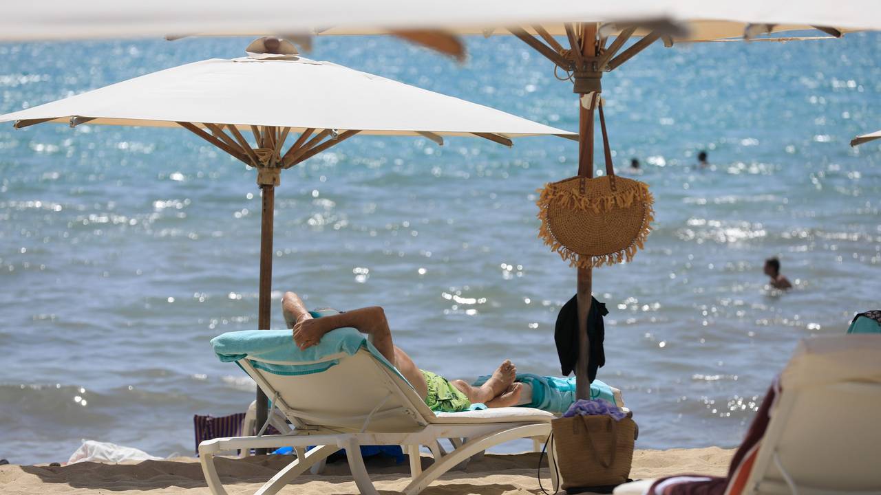 Menschen sonnen sich Mitte Juli am Strand von Arenal und baden im Meer an einem warmen Sommertag.
