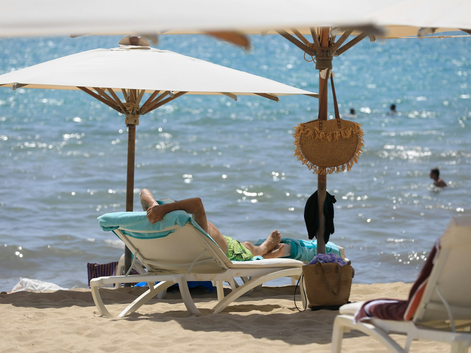 Menschen sonnen sich Mitte Juli am Strand von Arenal und baden im Meer an einem warmen Sommertag.