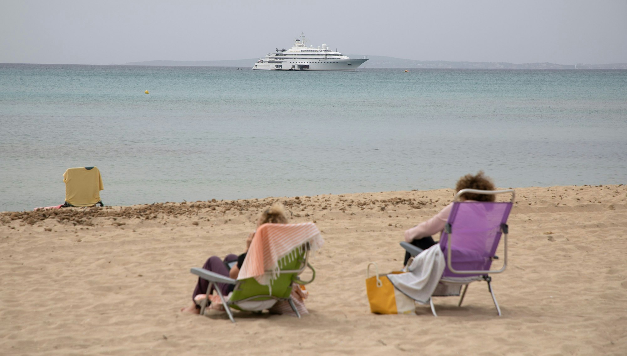 Frauen sitzen an einem bewölkten Tag am Strand von Arenal auf Mallorca zu Beginn der Osterferien.