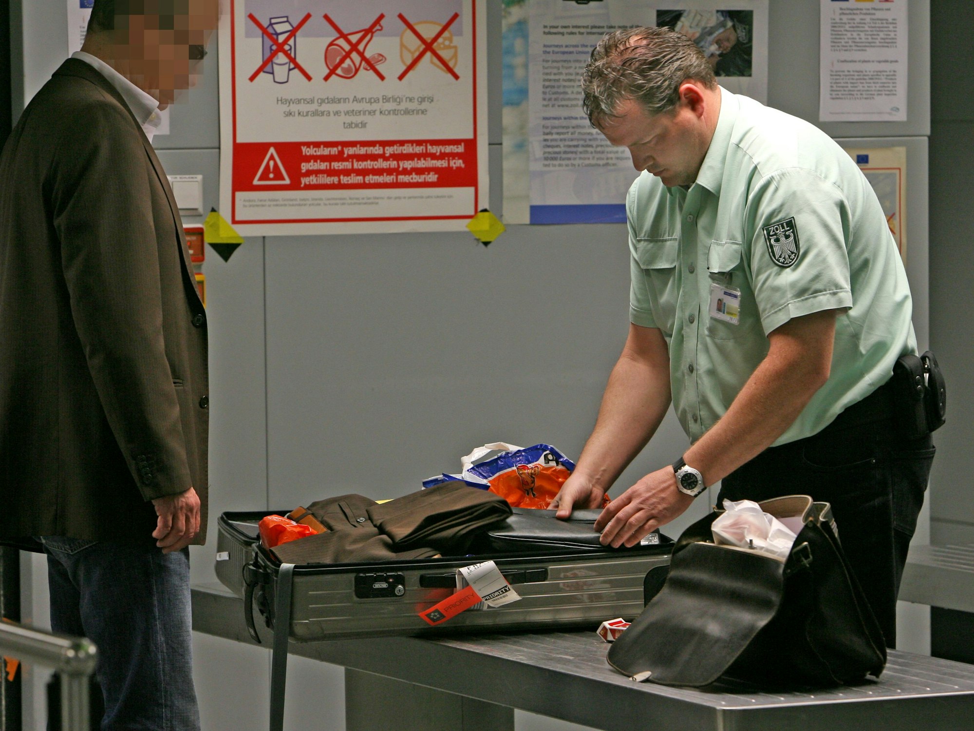 Akribisch durchsucht ein Zollbeamter den Koffer eines Reisenden.