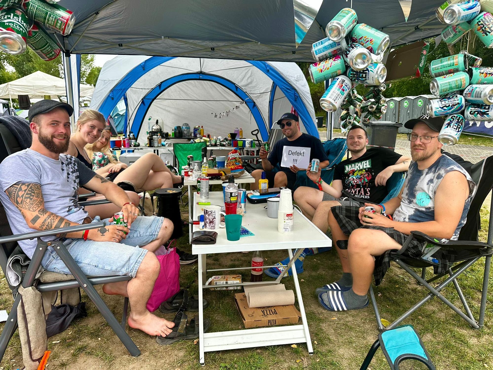 Tim und seine Freunde sitzen an ihrem Campingtisch und lächeln in die Kamera.