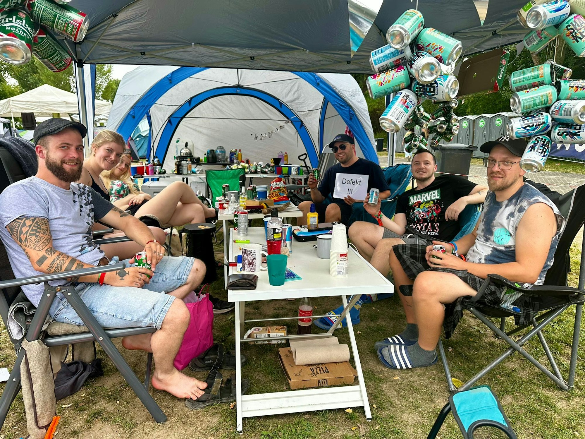 Tim und seine Freunde sitzen an ihrem Campingtisch und lächeln in die Kamera.