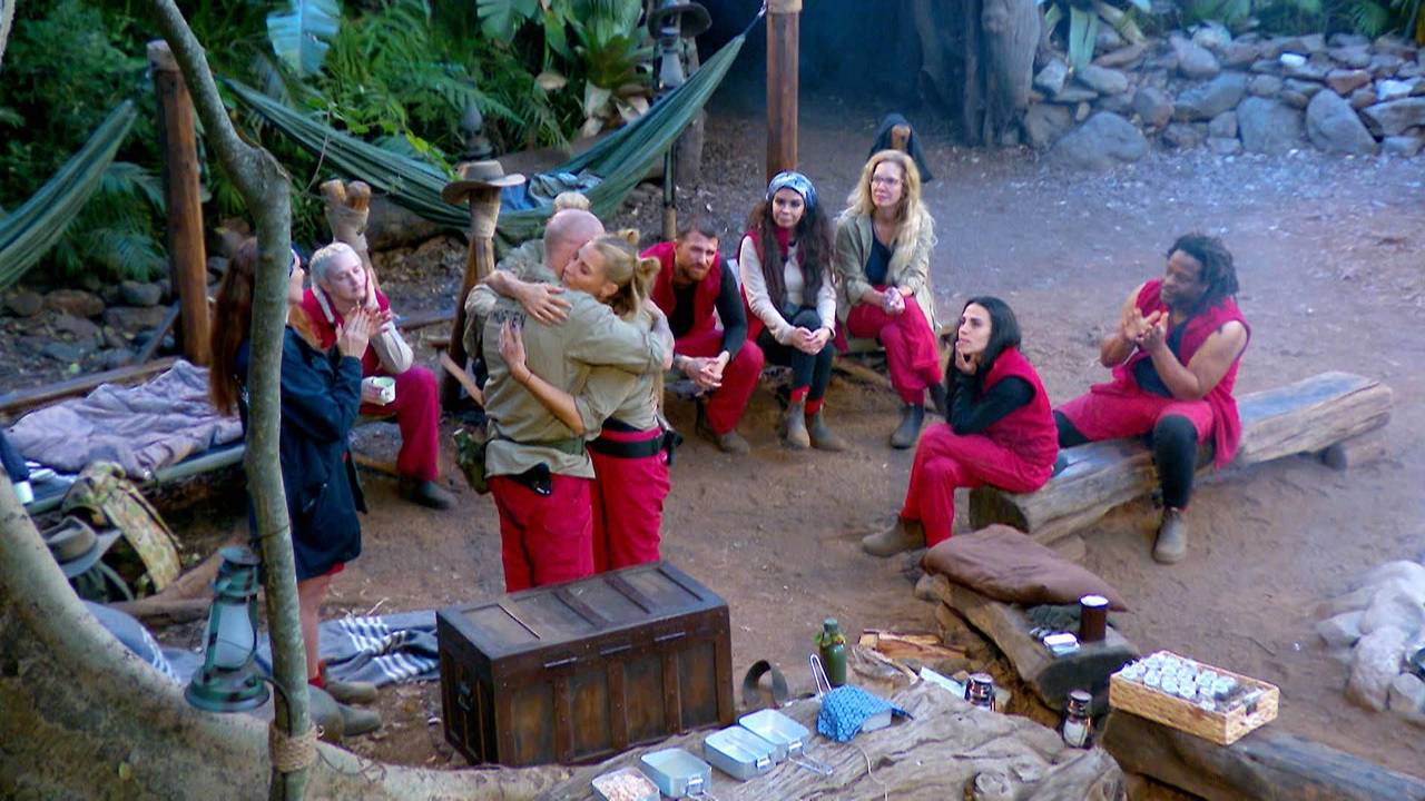 Thorsten Legat und Giulia Siegel umarmen sich vor den restlichen Teilnehmenden im Dschungelcamp.