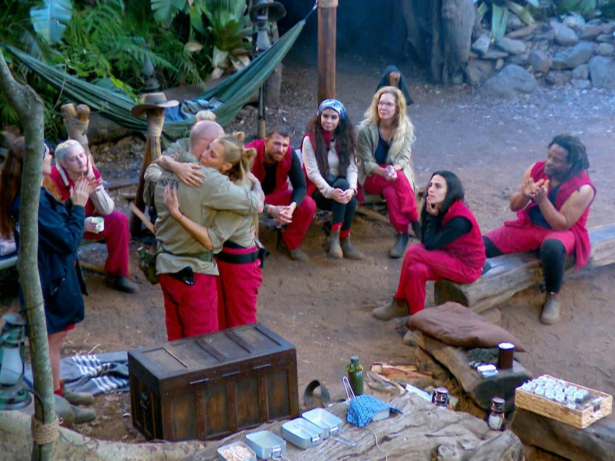 Thorsten Legat und Giulia Siegel umarmen sich vor den restlichen Teilnehmenden im Dschungelcamp.