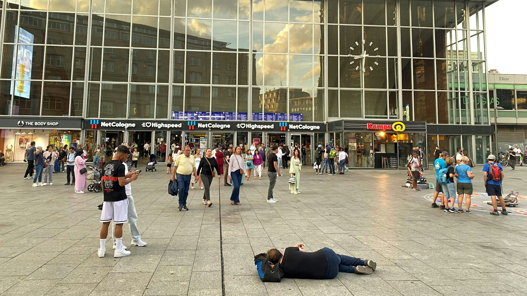 Mann liegt auf dem Steinboden zwischen Kölner Hauptbahnhof und Kölner Dom.