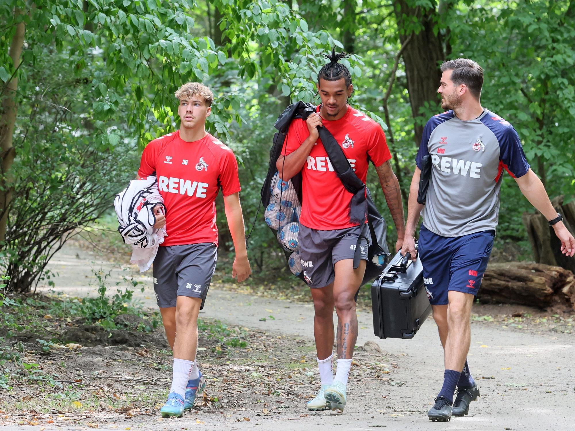 Meiko Wäschenbach und Damion Downs tragen Leibchen und Bälle zum Training. Neben ihnen geht Max Weuthen.
