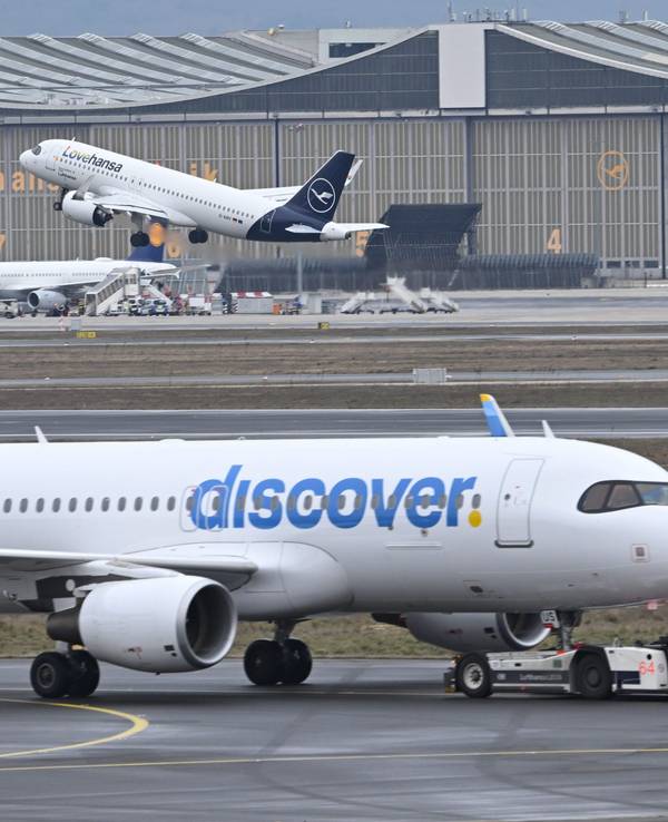 ARCHIV - 14.02.2024, Hessen, Frankfurt/Main: Während eine Maschine der Lufthansa startet, wird ein Passagierflugzeug der Discover Airlines am Frankfurter Flughafen von einem Schlepper gezogen. (zu dpa: «Gewerkschaften rufen Crews bei Lufthansa-Tochter zum Streik») Foto: Arne Dedert/dpa +++ dpa-Bildfunk +++