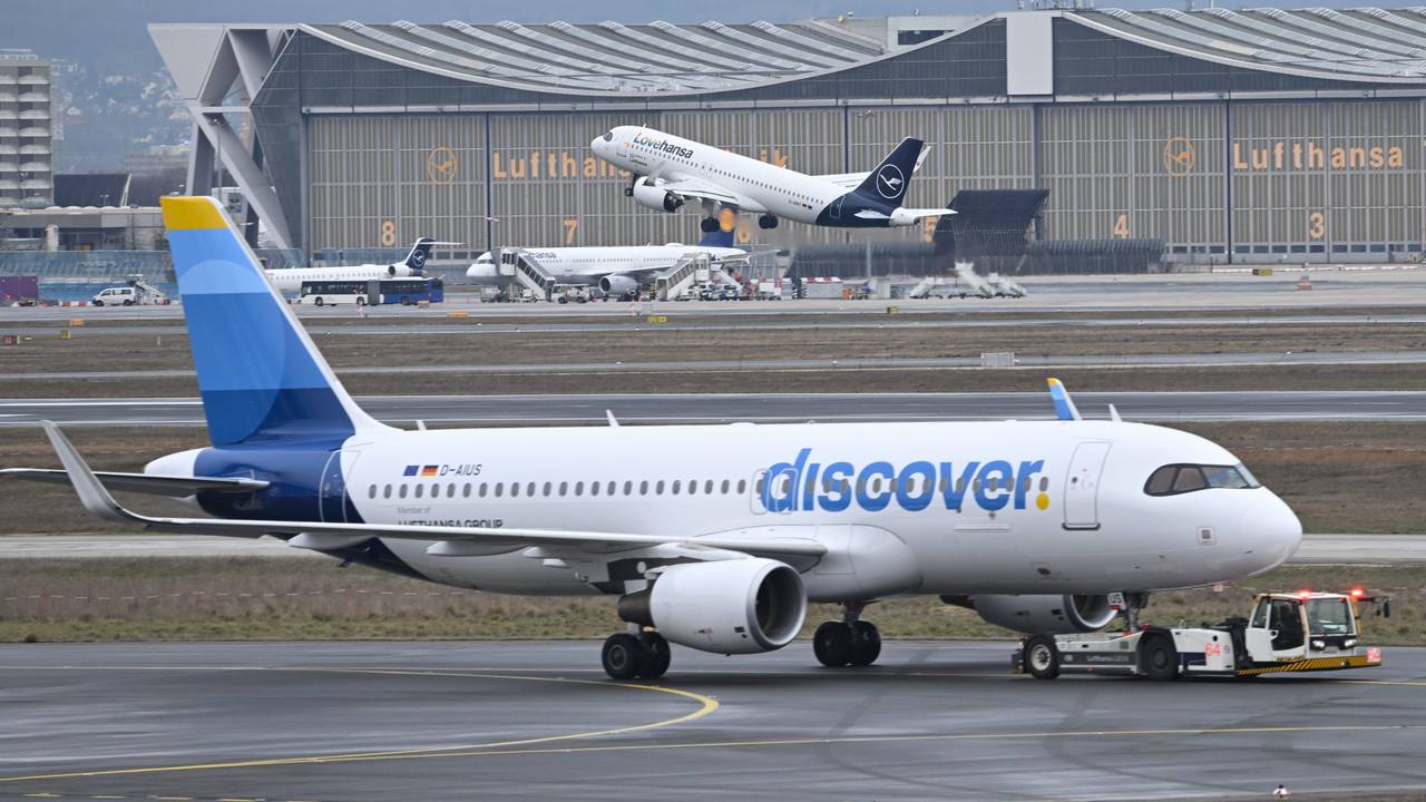 ARCHIV - 14.02.2024, Hessen, Frankfurt/Main: Während eine Maschine der Lufthansa startet, wird ein Passagierflugzeug der Discover Airlines am Frankfurter Flughafen von einem Schlepper gezogen. (zu dpa: «Gewerkschaften rufen Crews bei Lufthansa-Tochter zum Streik») Foto: Arne Dedert/dpa +++ dpa-Bildfunk +++