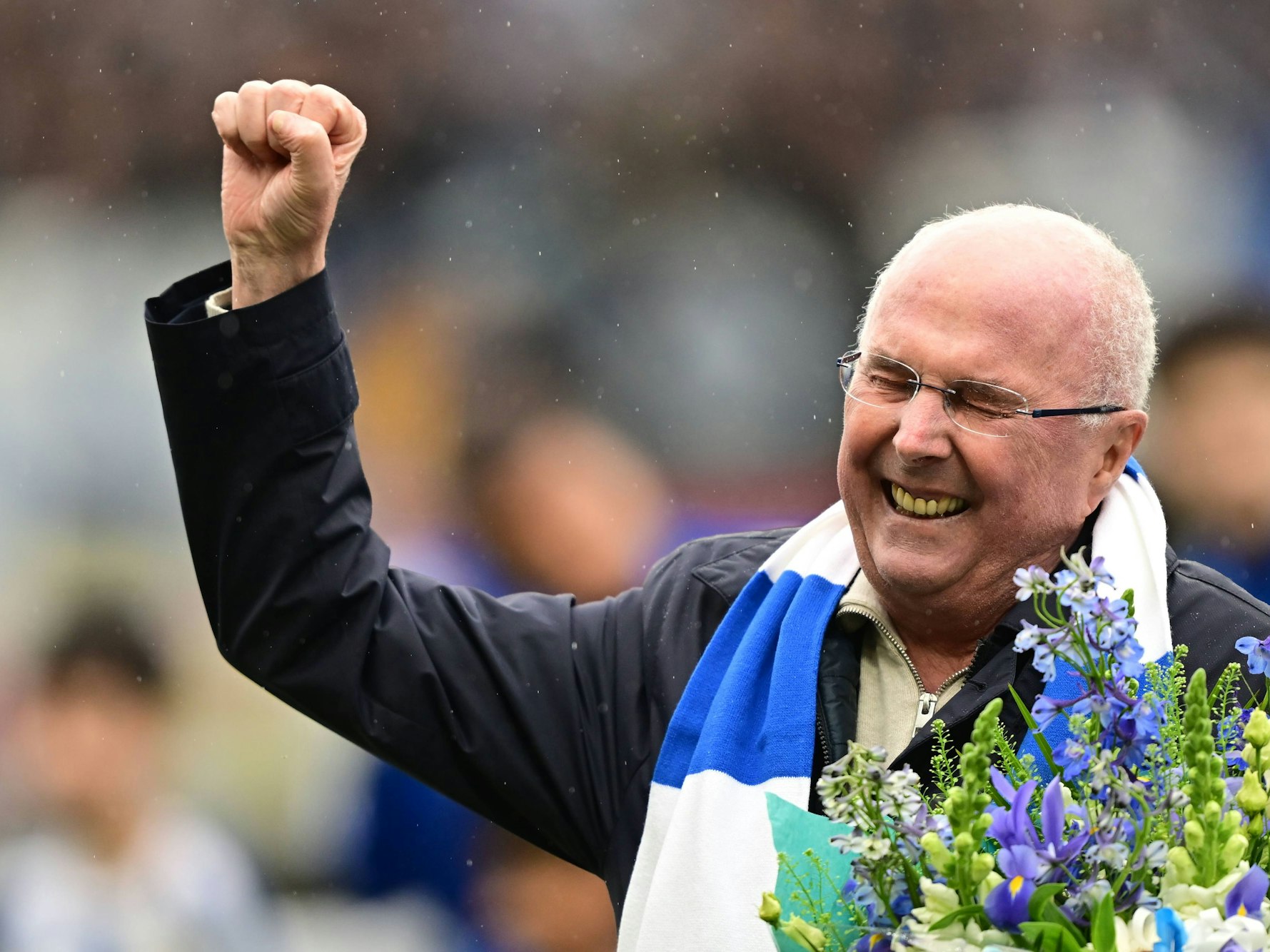 Sven-Göran Eriksson hat Blumen in der Hand und reckt die Faust nach oben.