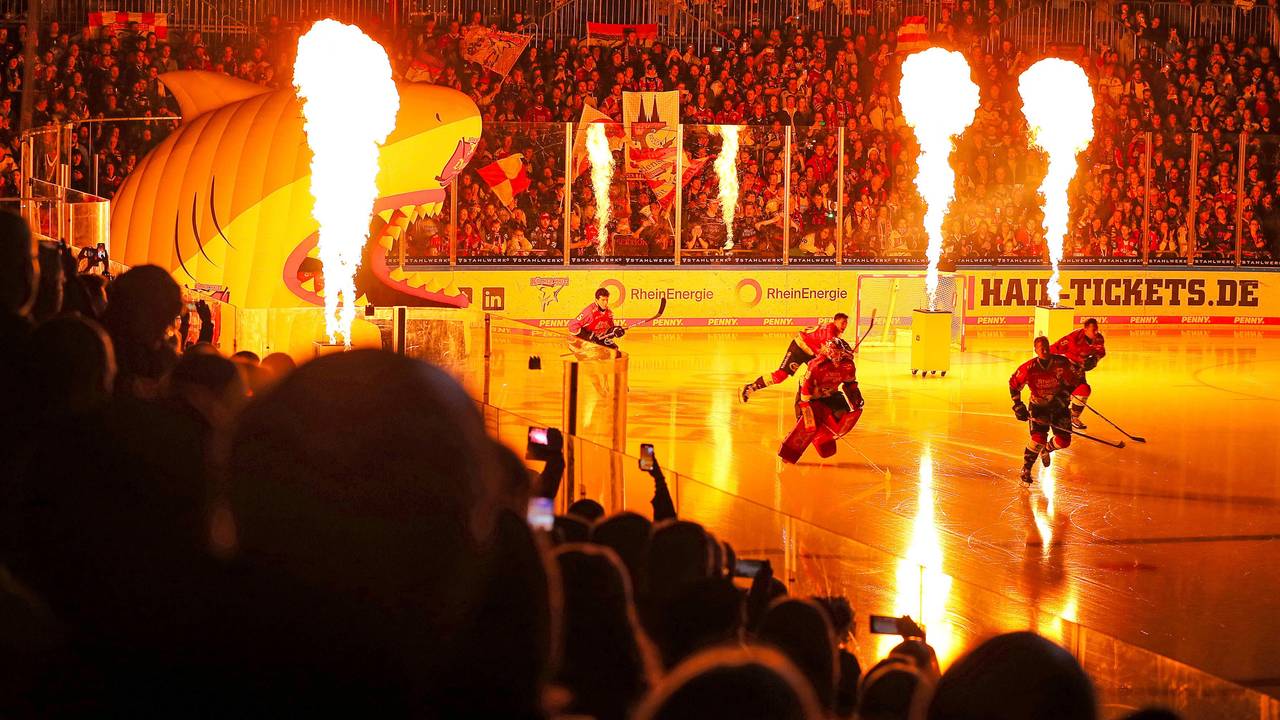 Die Spieler der Kölner Haie stürmen in der Lanxess-Arena vor einem DEL-Spiel aufs Eis.