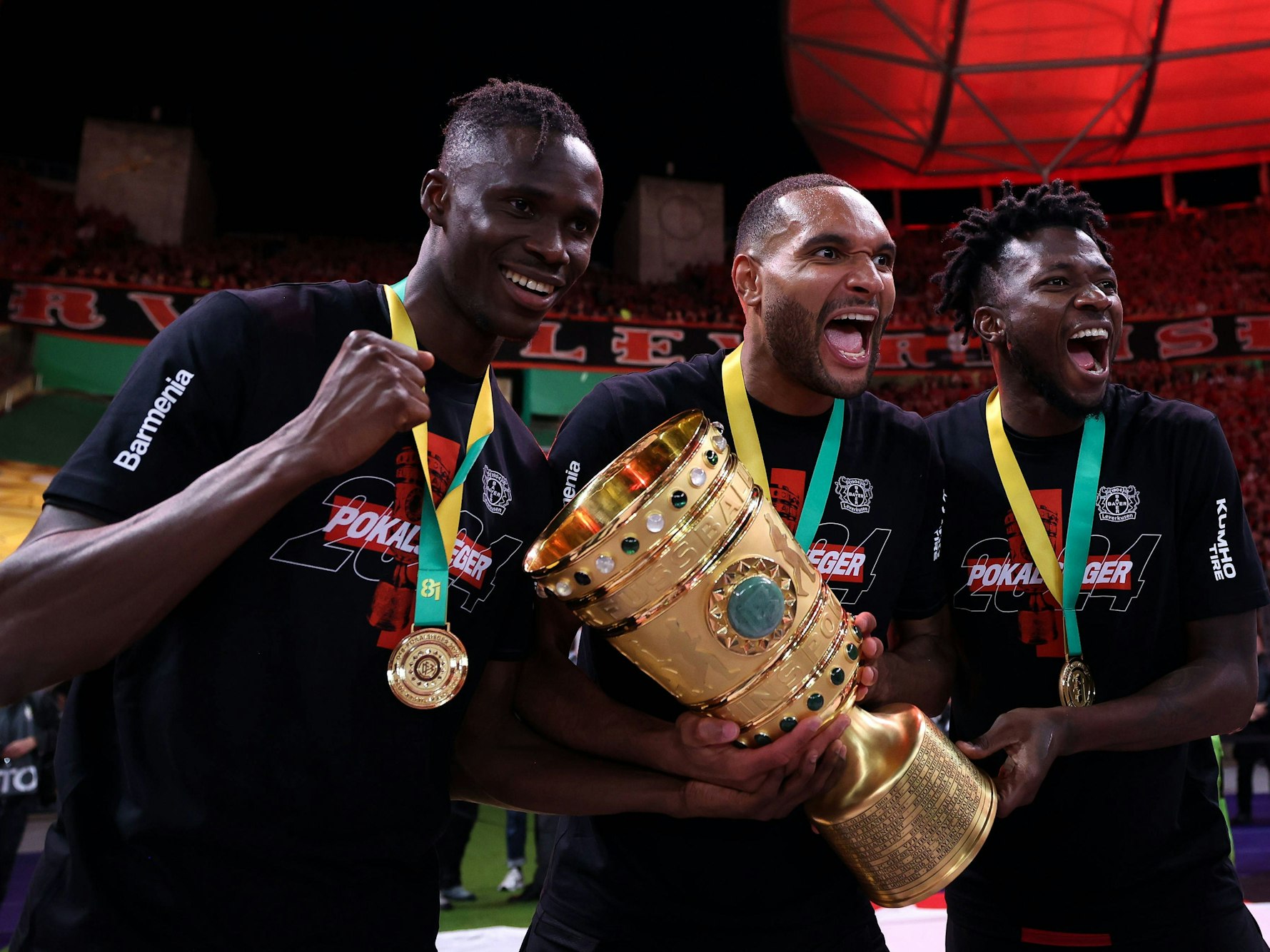 Odilon Kossounou (l.), Jonathan Tah (M.) und Edmond Tapsoba jubeln mit dem Pokal in den Händen.