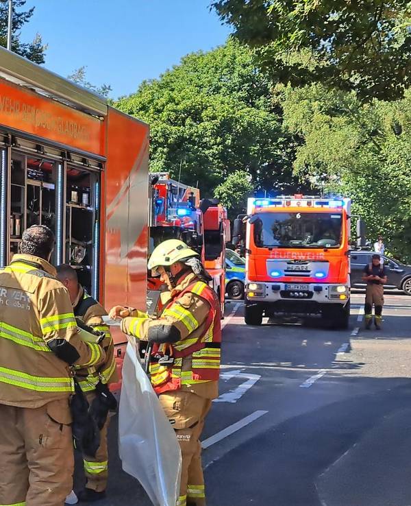 Drei Feuerwehrleute stehen an einem Löschfahrzeug, dahinter stehen weitere Löschfahrzeuge.