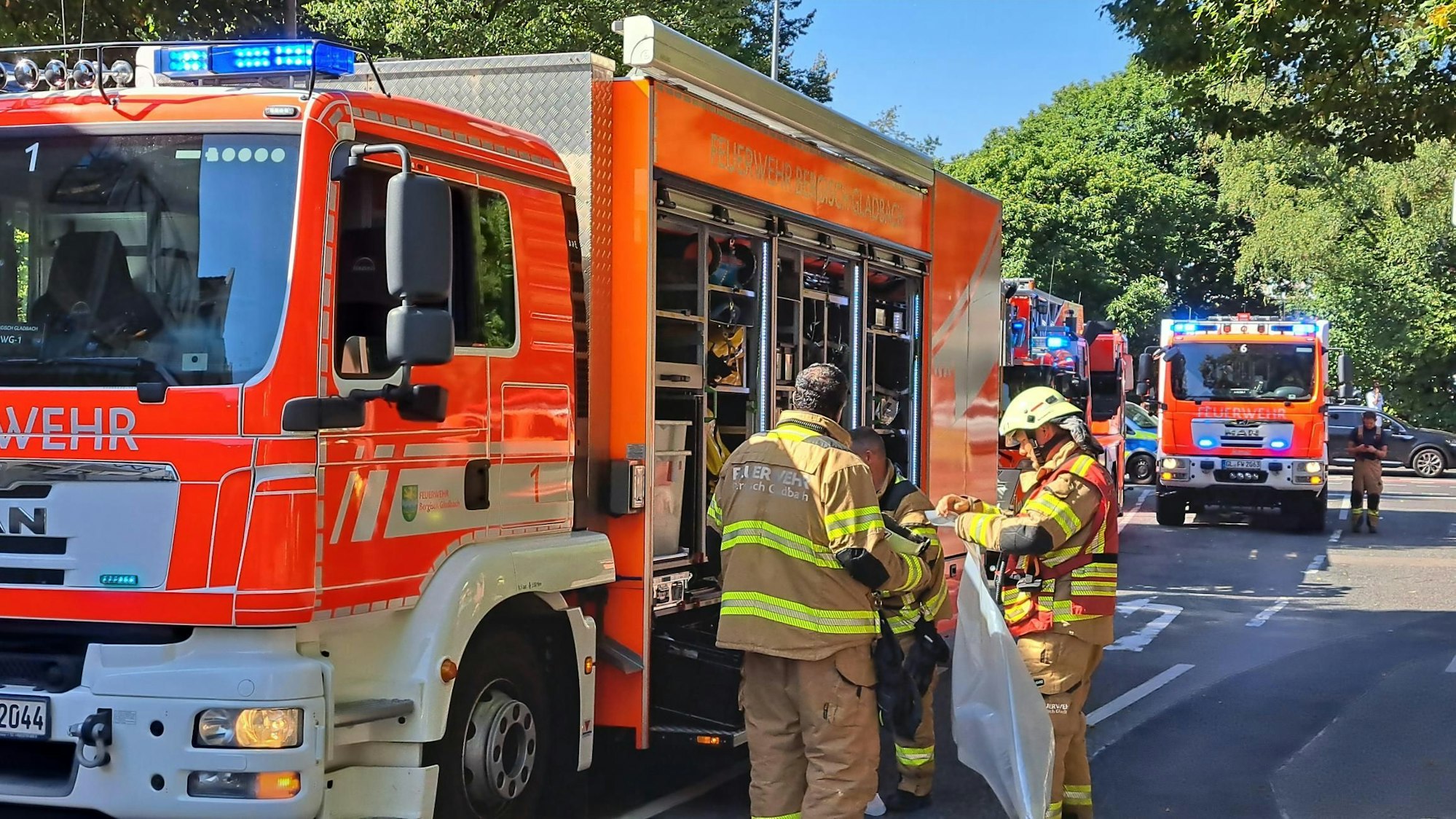 Drei Feuerwehrleute stehen an einem Löschfahrzeug, dahinter stehen weitere Löschfahrzeuge.
