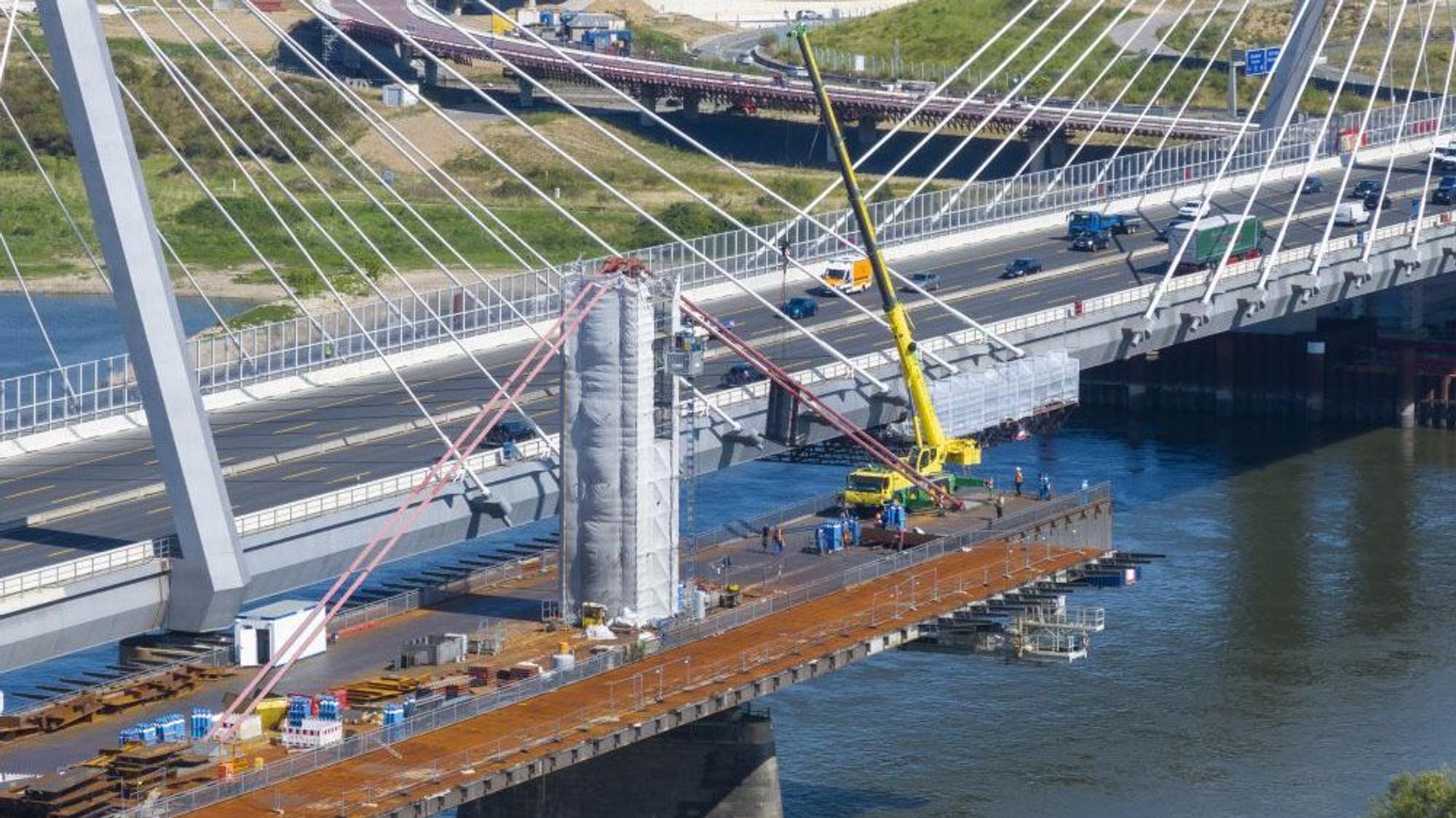 Ein Kran steht auf einer bereits zur Hälfte demontierten Brücke, daneben fahren Fahrzeuge über eine neue Brücke.