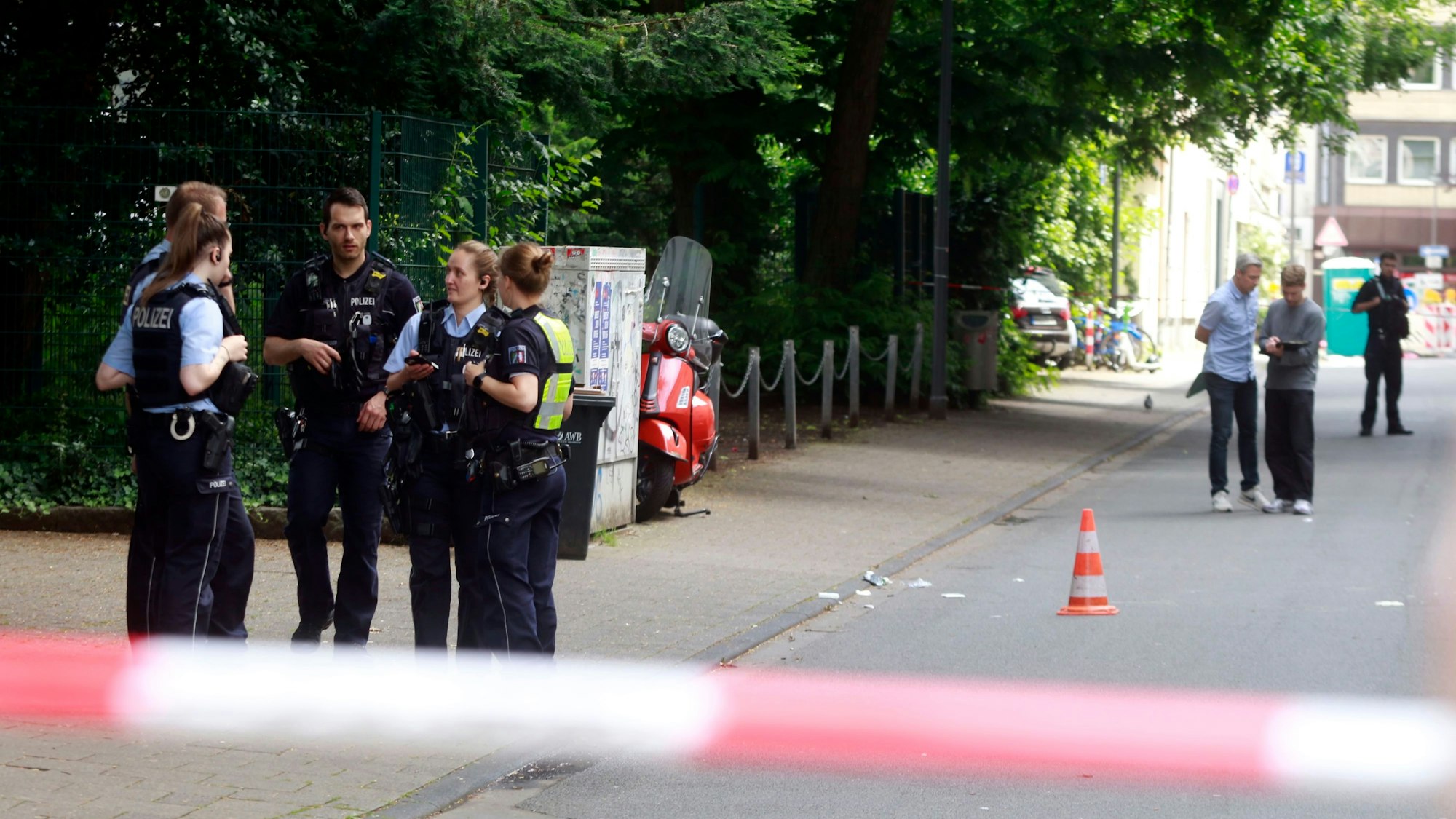 Polizeikräfte stehen an einem Tatort, der mit Flatterband abgesperrt ist.
