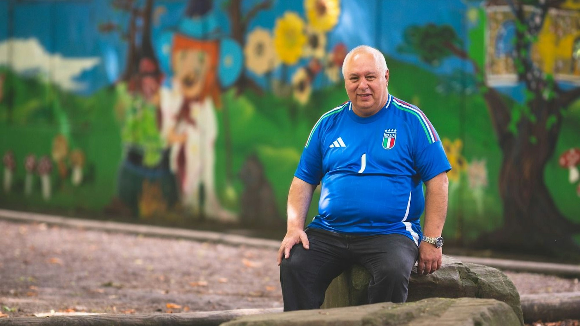 Antonio Pizzulli sitzt auf einem Stein vor einer bemalten Wand.