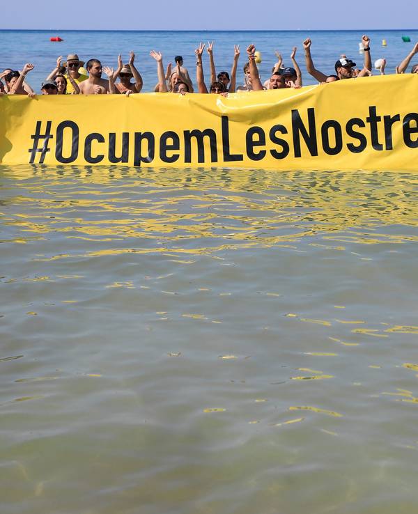 Leute halten an einem Strand auf Mallorca ein Banner „#Besetzen wir unsere Strände“ aus Protest gegen den Massentourismus auf der Balearen-Insel.