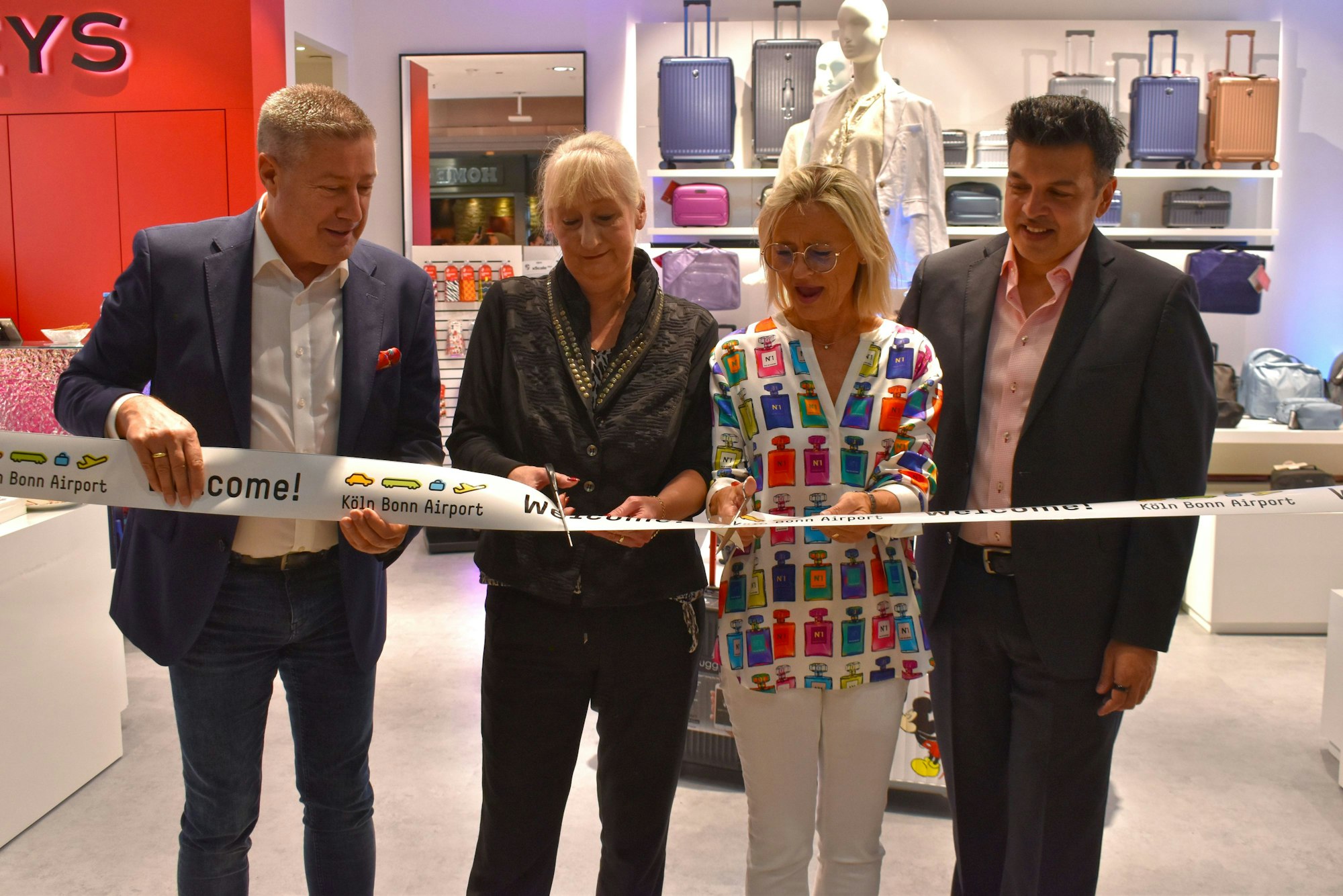 Zwei Männer und zwei Frauen stehen hinter einem Band mit der Aufschrift „Köln Bonn Airport“. Eine der Frauen ist gerade dabei, das Band mit einer Schere zu durchschneiden.