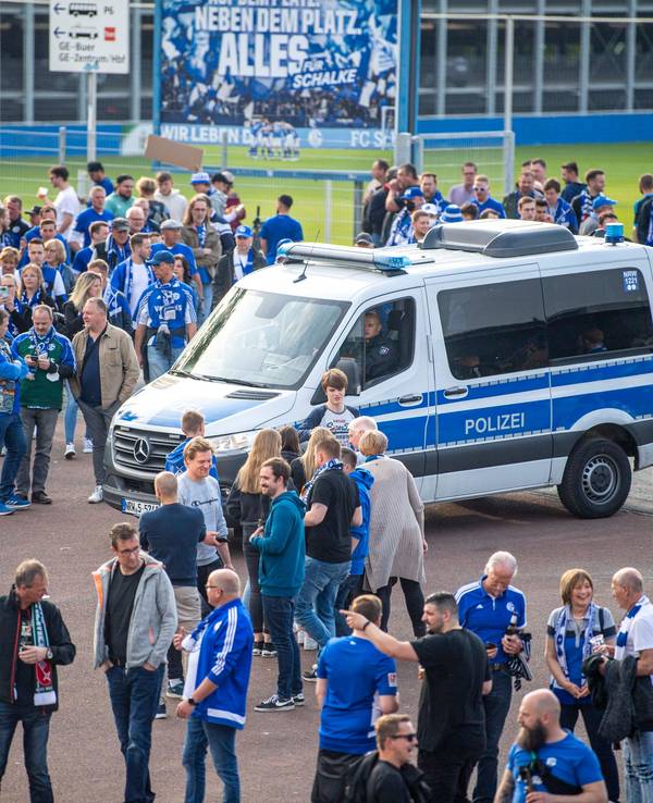 Ein Polizeiwagen steht vor der Veltins-Arena, darum stehen zahlreiche Schalke-Fans.