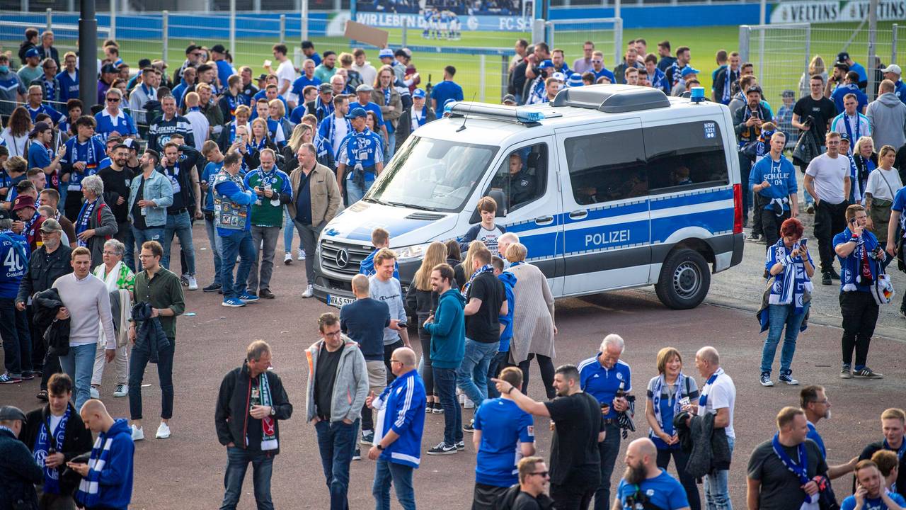 Ein Polizeiwagen steht vor der Veltins-Arena, darum stehen zahlreiche Schalke-Fans.
