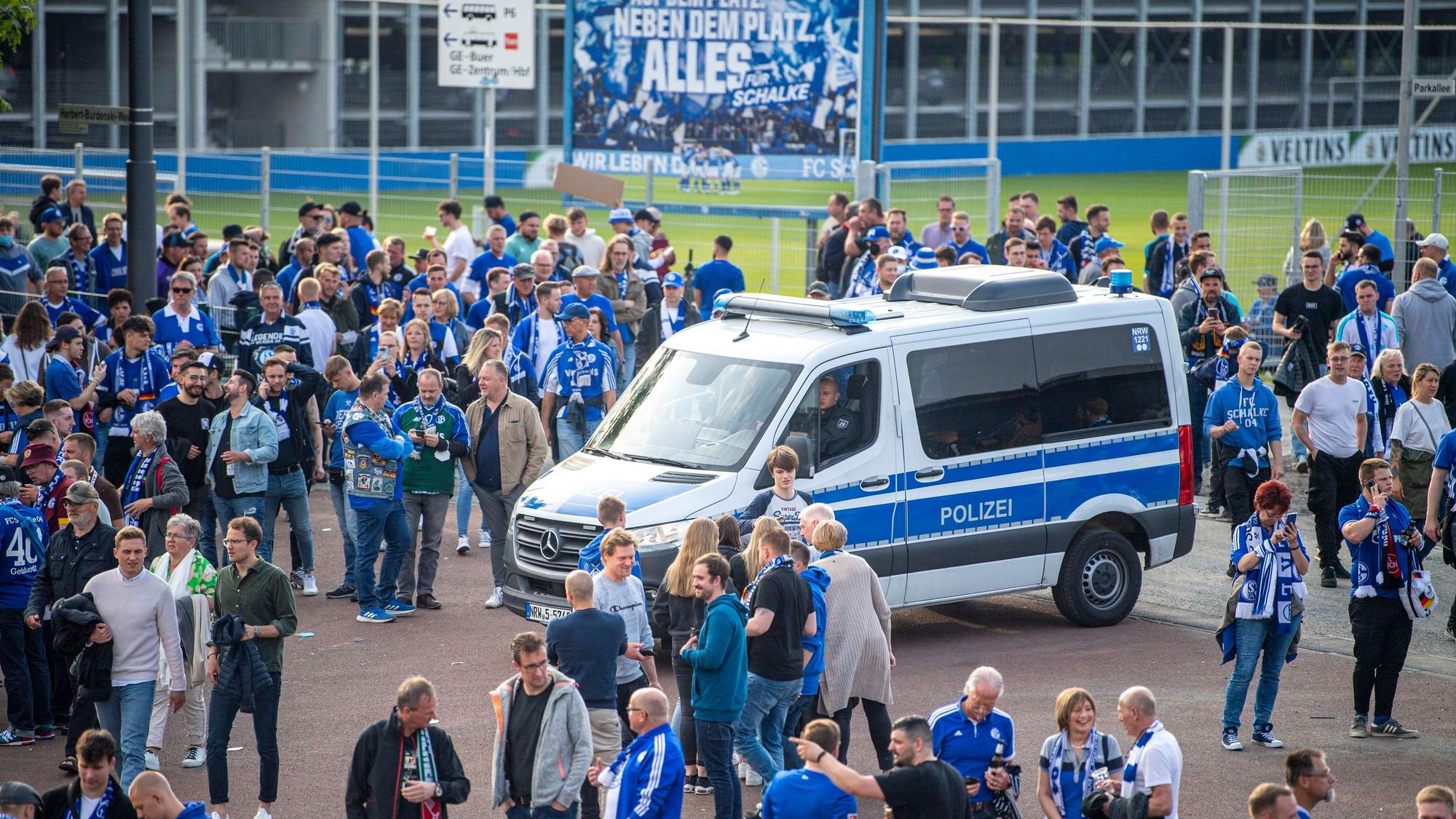 Ein Polizeiwagen steht vor der Veltins-Arena, darum stehen zahlreiche Schalke-Fans.