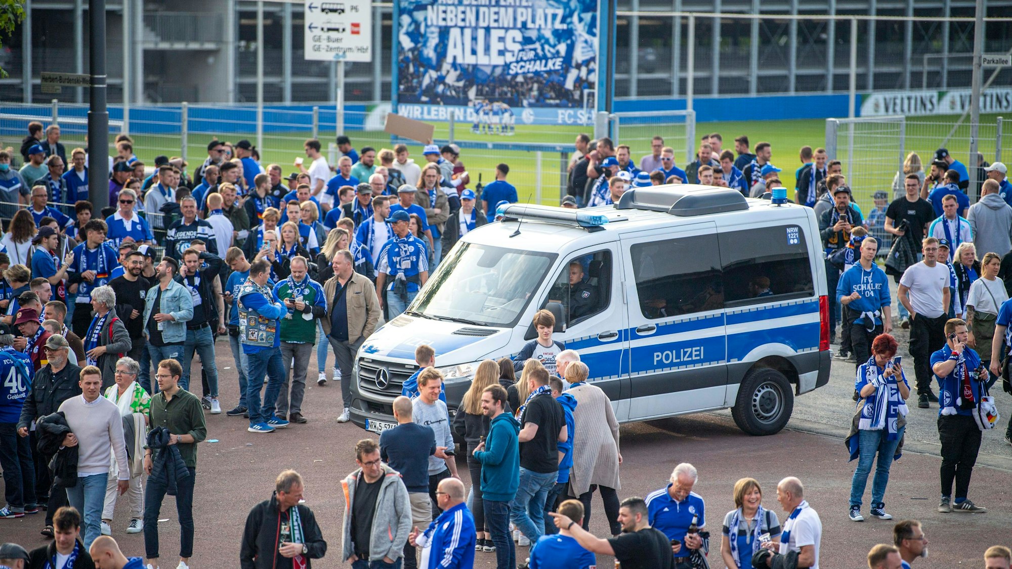 Ein Polizeiwagen steht vor der Veltins-Arena, darum stehen zahlreiche Schalke-Fans.