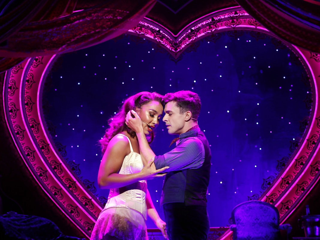 Ein Paar steht singend auf der Bühne vor einem großen, beleuchteten Herz.