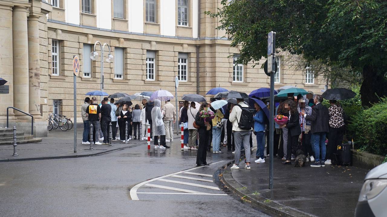 Zahlreiche Menschen stehen draußen vor dem Kölner Oberlandesgericht, einige haben Blumensträuße mitgebracht.