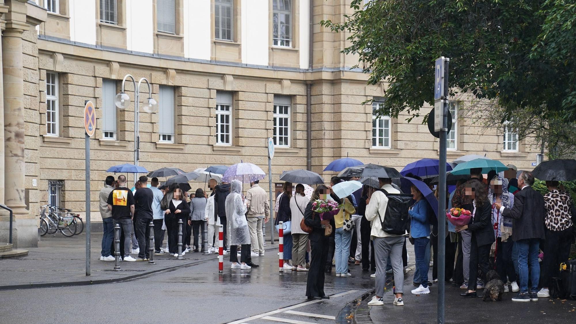Zahlreiche Menschen stehen draußen vor dem Kölner Oberlandesgericht, einige haben Blumensträuße mitgebracht.
