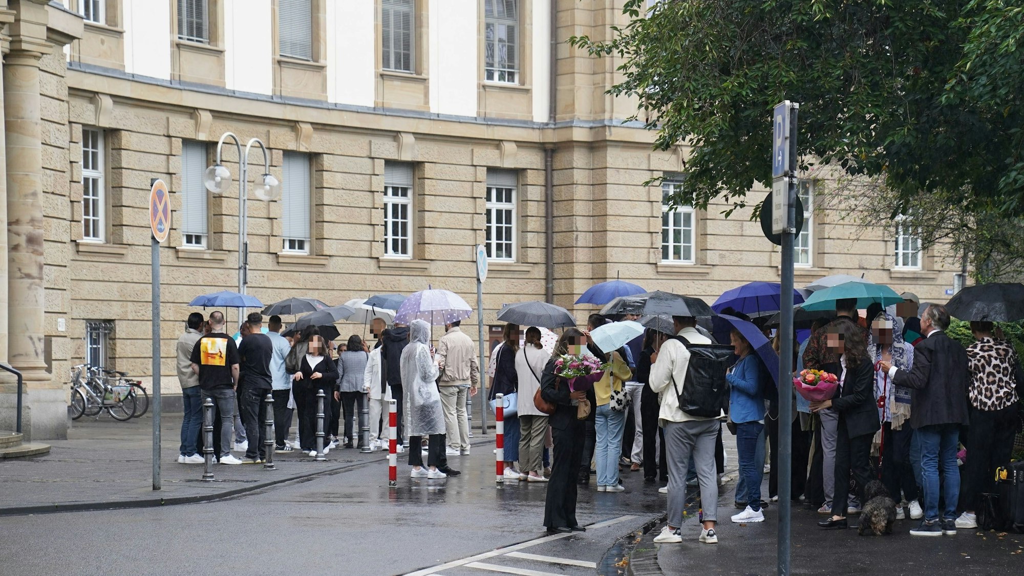 Zahlreiche Menschen stehen draußen vor dem Kölner Oberlandesgericht, einige haben Blumensträuße mitgebracht.