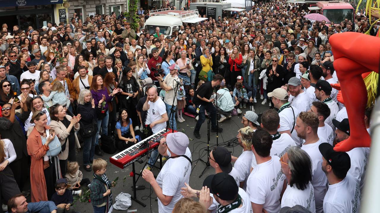 Menschenmassen stehen auf einem Platz um einen Chor herum.
