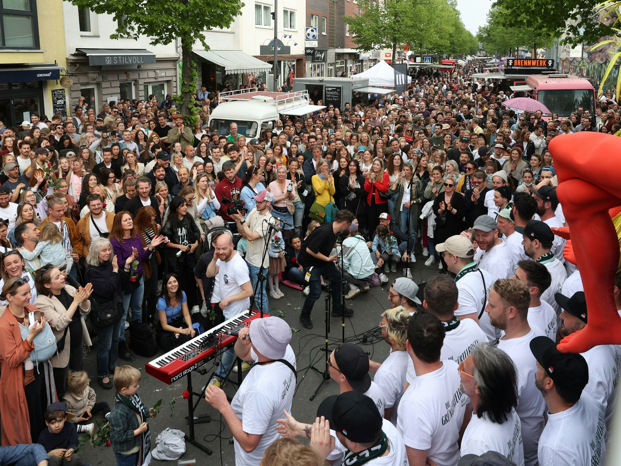 Menschenmassen stehen auf einem Platz um einen Chor herum.