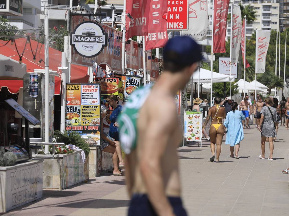 Menschen spazieren an Bars vorbei an einer Promenade in Magaluf.