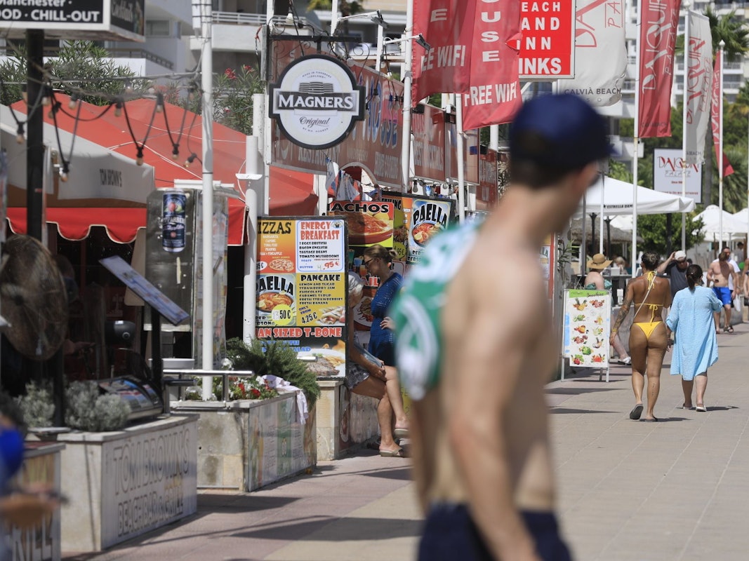 Menschen spazieren an Bars vorbei an einer Promenade in Magaluf.