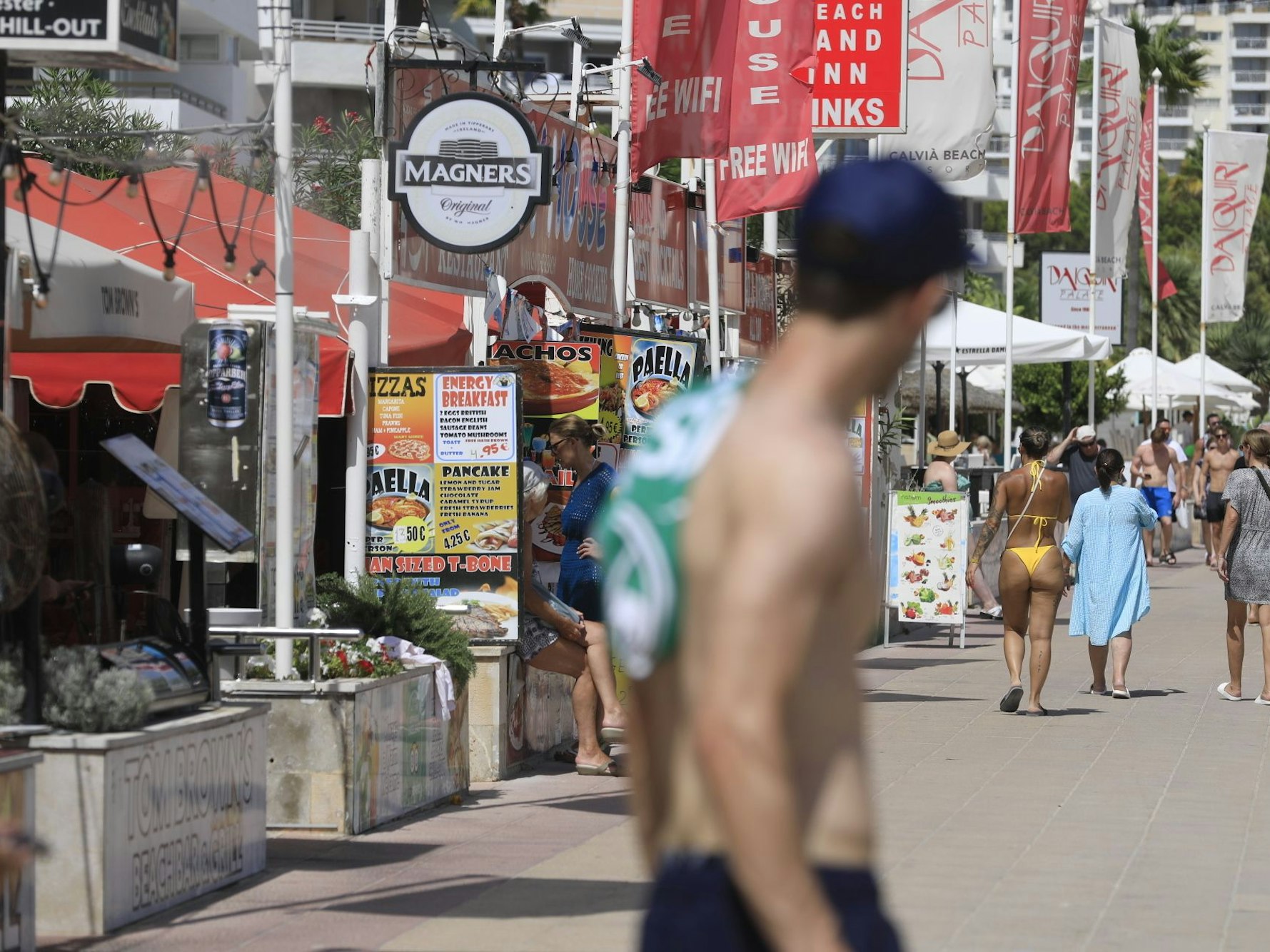 Menschen spazieren an Bars vorbei an einer Promenade in Magaluf.
