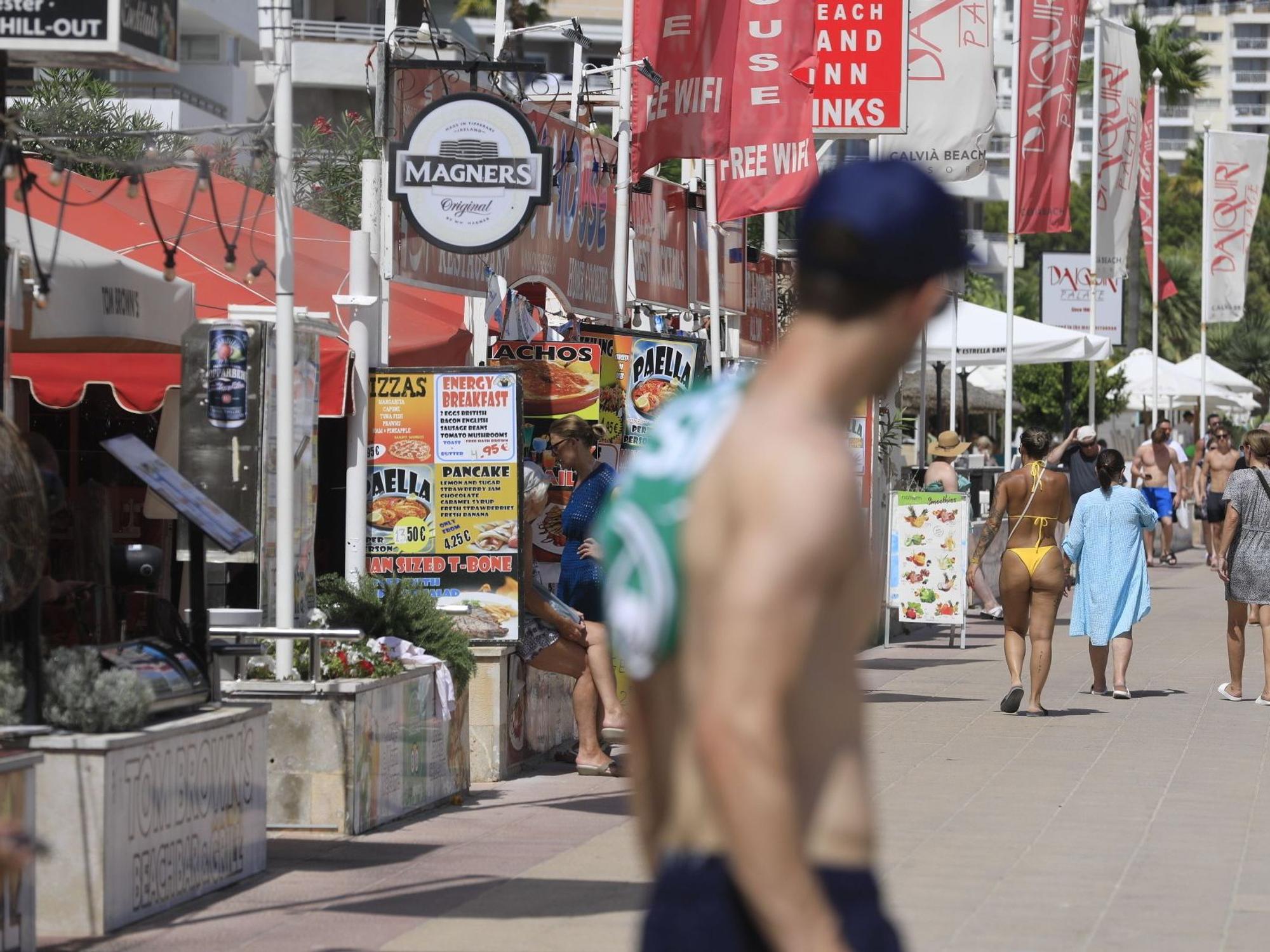Menschen spazieren an Bars vorbei an einer Promenade in Magaluf.