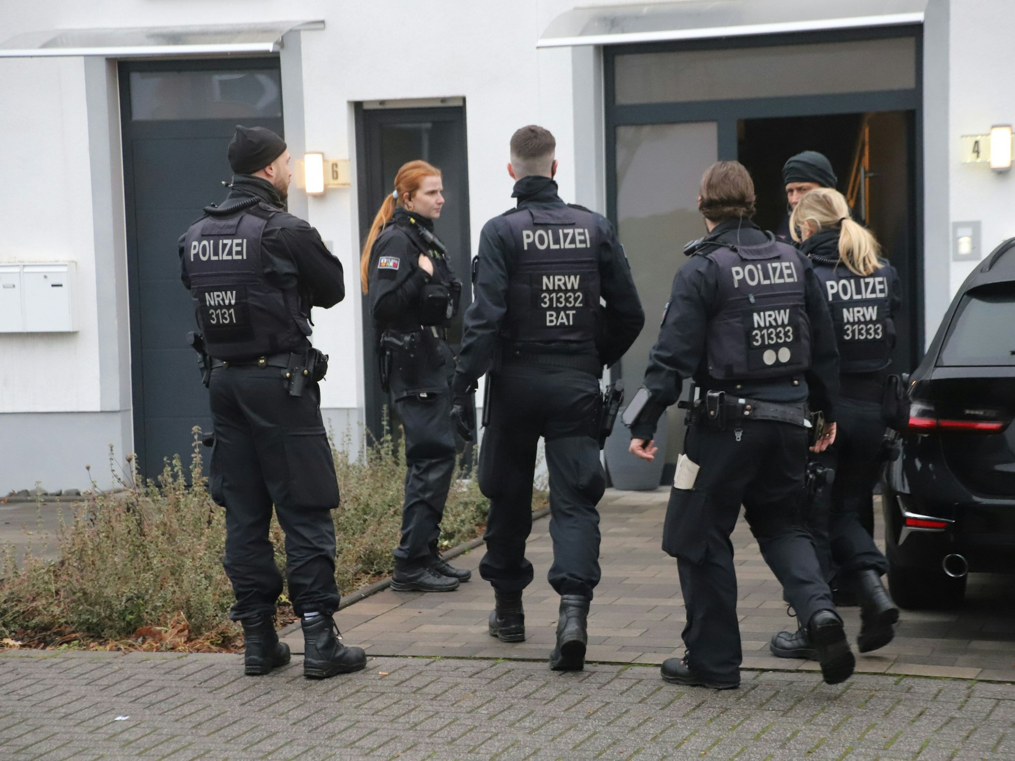 Sechs Einsatzkräfte der Polizei stehen vor einem Hauseingang.