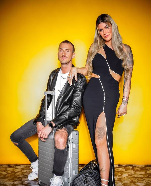 Das Foto zeigt Gloria Glumac und ihren Freund Michael vor einer gelben Wand. Sie steht, er sitzt auf einem Koffer.