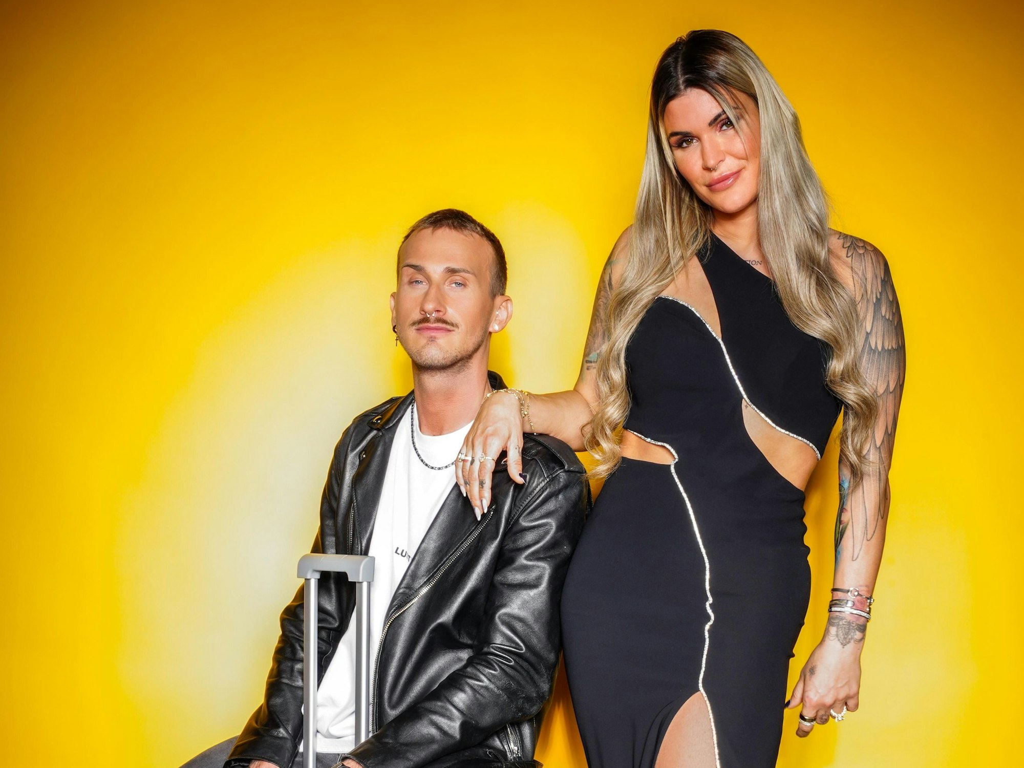 Das Foto zeigt Gloria Glumac und ihren Freund Michael vor einer gelben Wand. Sie steht, er sitzt auf einem Koffer.